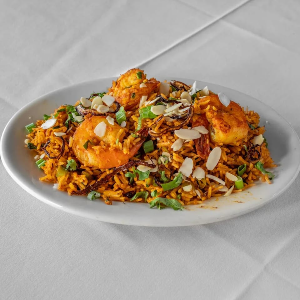Raga Indian Cuisine's shrimp biryani, a vibrant orange rice dish with large shrimp, almonds, and herbs.