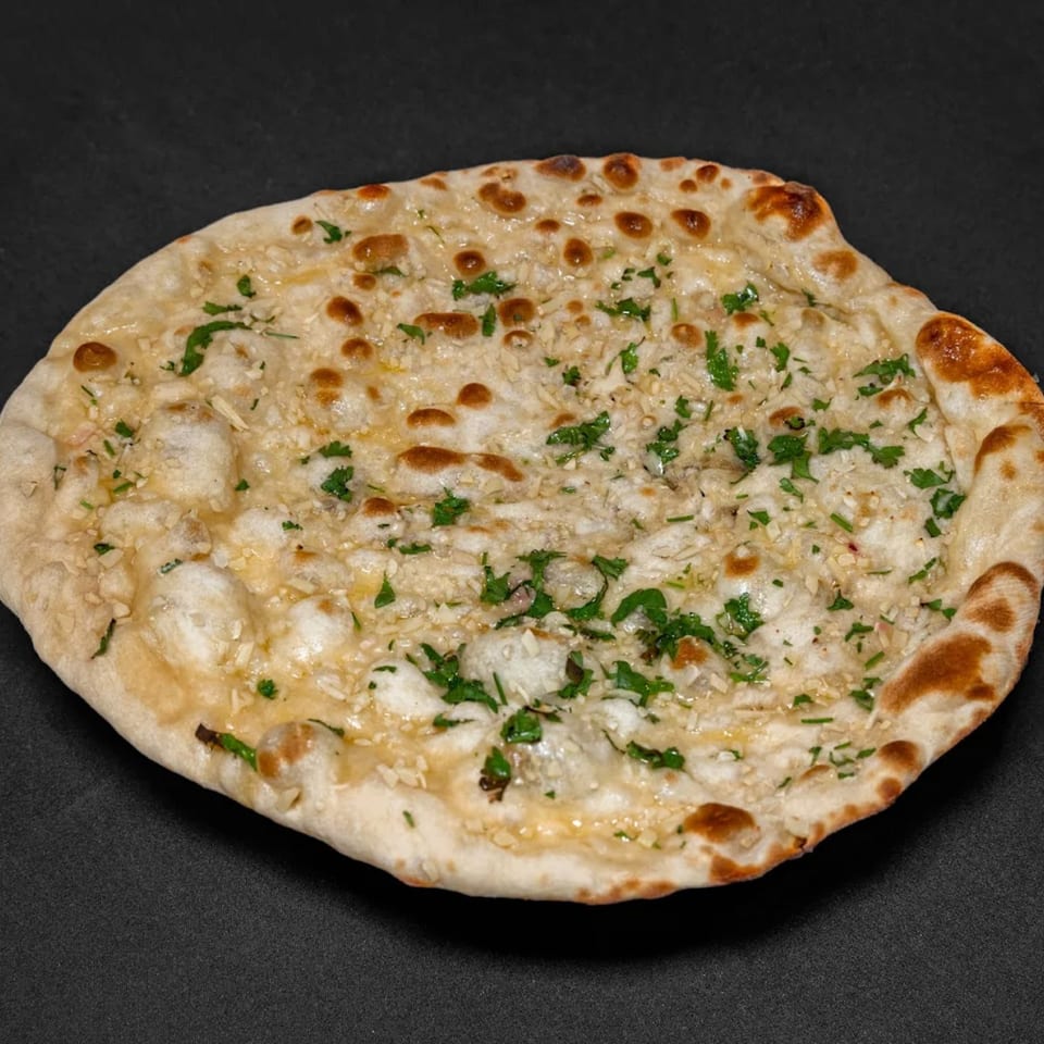 A close-up of Raga Indian Cuisine's garlic naan, topped with fresh herbs and minced garlic.