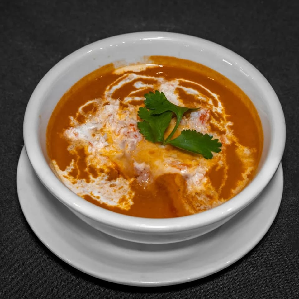 A white bowl of Raga Indian Cuisine's orange soup, swirled with cream and garnished with cilantro.