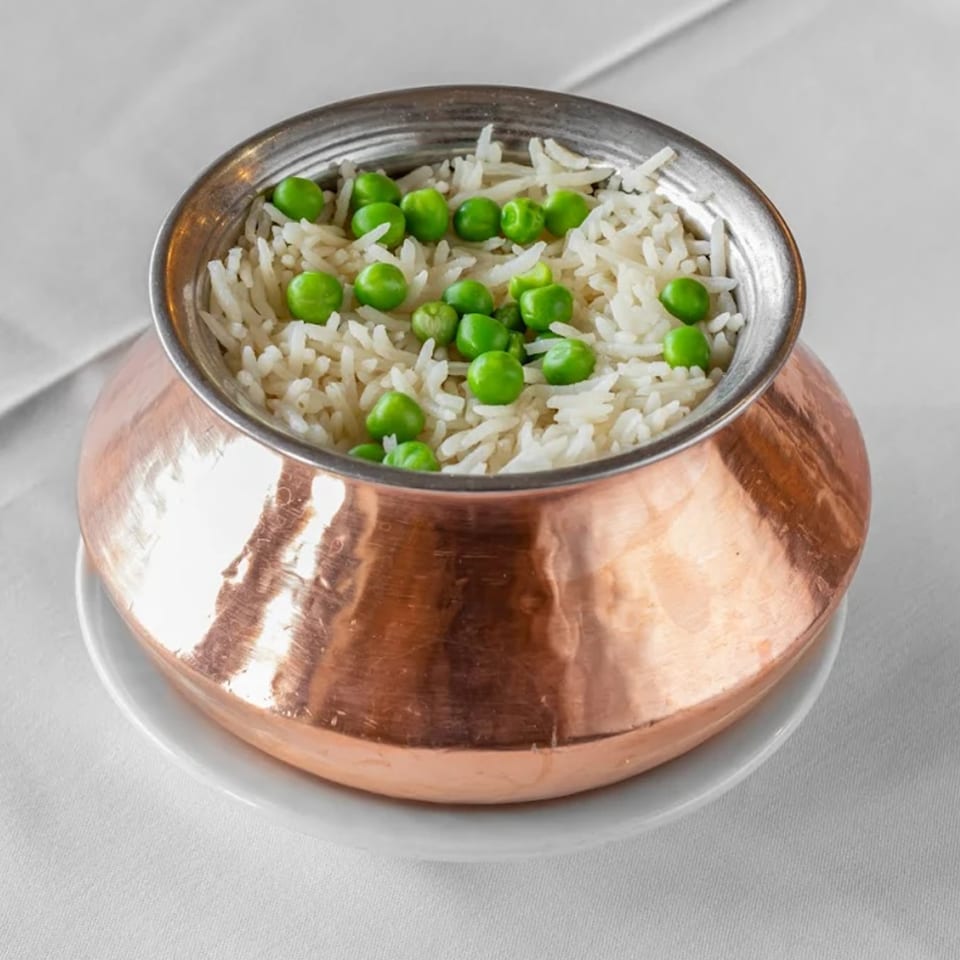 Peas Pulao, white rice with green peas, served in a hammered copper bowl on a white tablecloth.