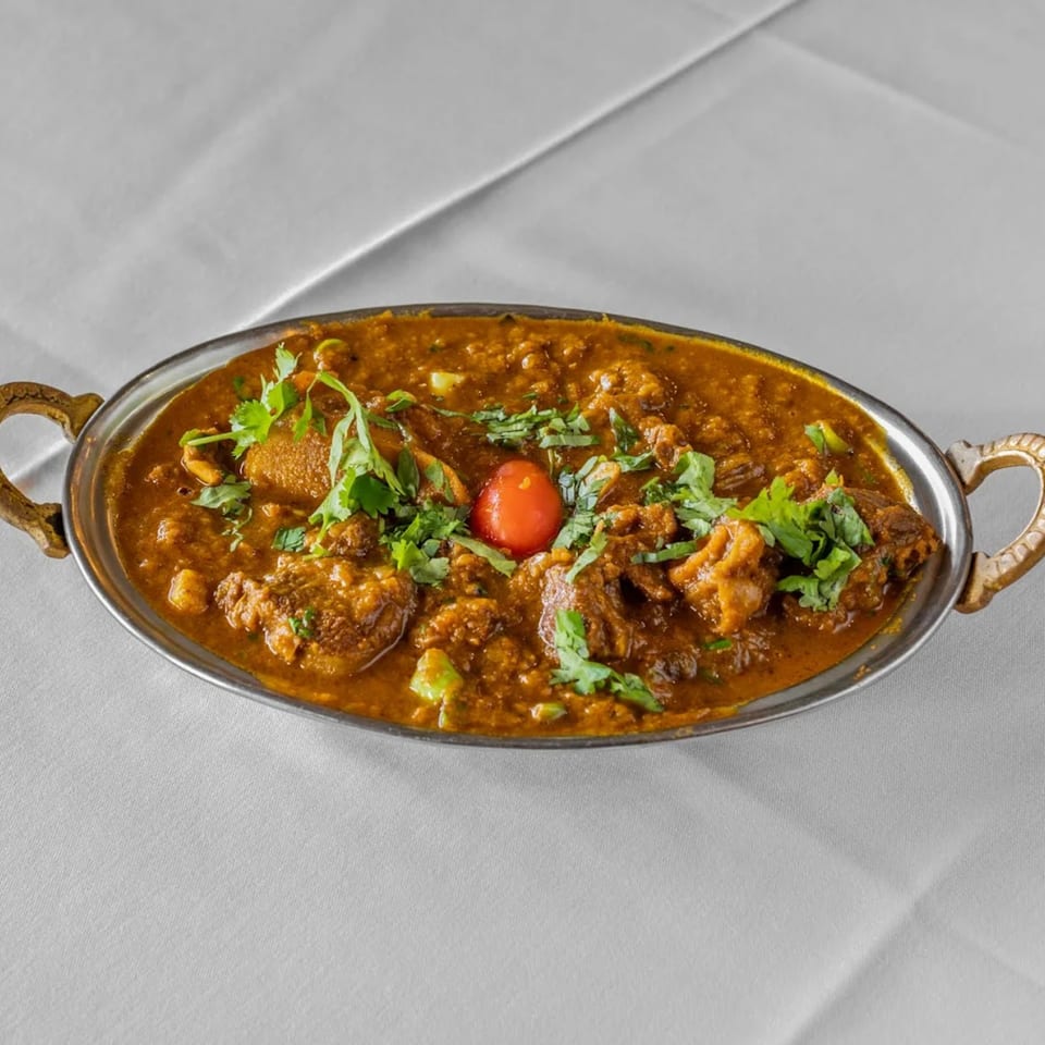 Raga Indian Cuisine's lamb curry, garnished with cilantro and a cherry tomato, in a silver serving dish.