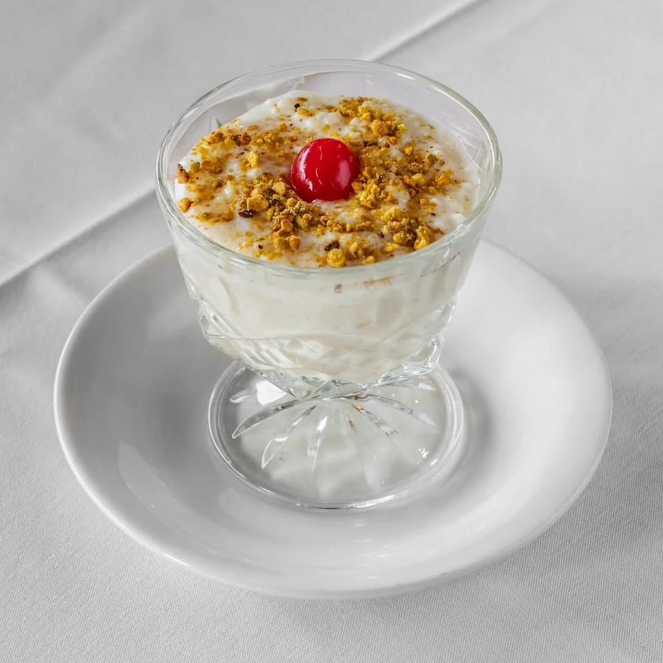 Indian rice pudding (kheer) in a glass, topped with crushed nuts and a red cherry.