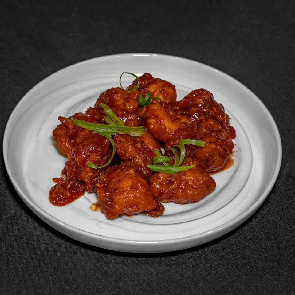 Raga Indian Cuisine's chili chicken, a vibrant red dish garnished with fresh green onions on a white plate.