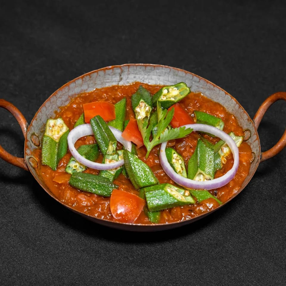 Raga Indian Cuisine's Bhindi Masala, a vibrant okra curry with tomatoes, onions, and cilantro in a copper karahi.